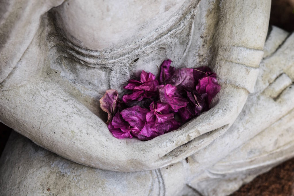 Seated meditative statue holding purple flower pedals.